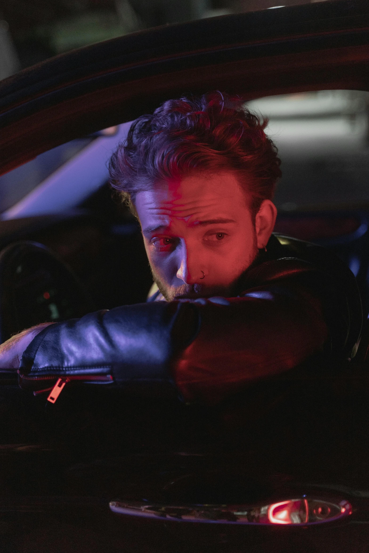 a man sitting in a car smoking a cigarette, an album cover, trending on pexels, photorealism, charlie cox, wearing leather jacket, high red lights, gif