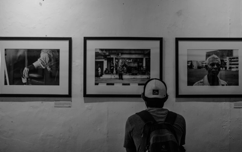a person standing in front of a wall with pictures on it, a black and white photo, pexels contest winner, visual art, people watching, exhibition of paintings, his whole head fits in the frame, monochrome:-2