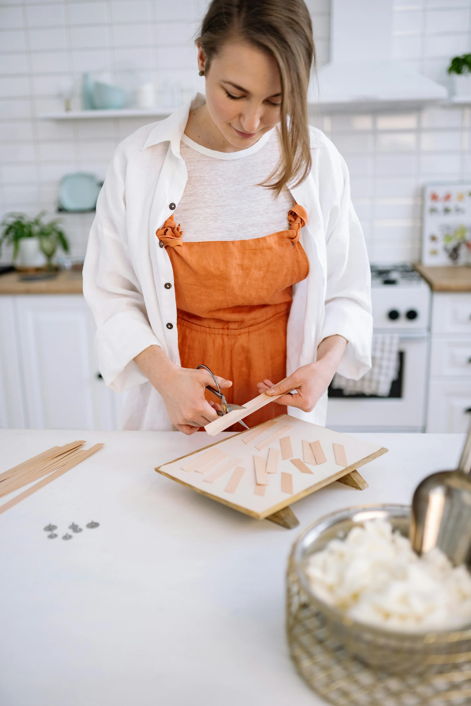 a woman in an orange apron preparing food in a kitchen, inspired by Yukimasa Ida, trending on pexels, arbeitsrat für kunst, made of wood, white, tabletop model, vanilla