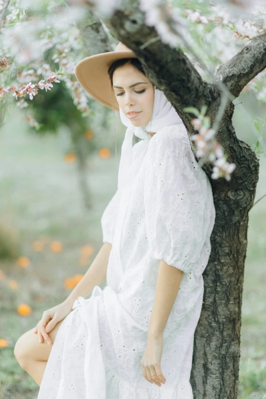 a woman in a white dress and hat sitting under a tree, inspired by Modest Urgell, unsplash, renaissance, puff sleeves, photoshoot for skincare brand, hooded, peach