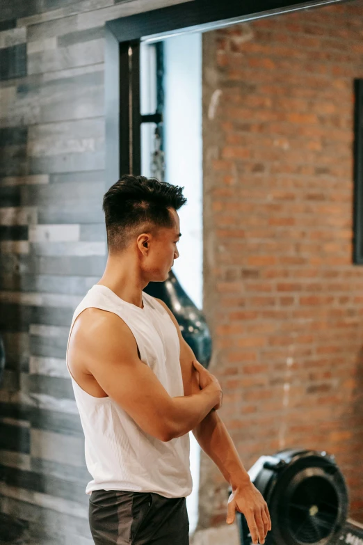a man standing in front of a mirror in a gym, trending on pexels, wearing : tanktop, darren quach, private moment, looking left
