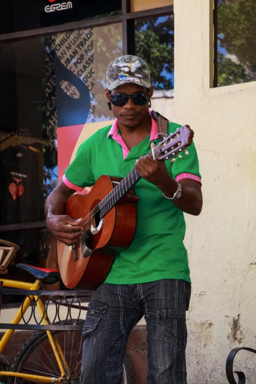 a man in a green shirt playing a guitar, inspired by Candido Bido, happening, wearing sunglasses and a cap, cuban setting, in town, multi colour