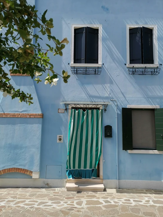 a blue building with a green and white striped chair in front of it, a picture, venice, profile image, apartment, door