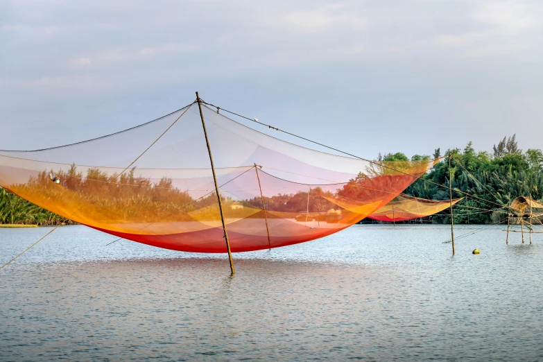 a large net sitting on top of a body of water, inspired by Christo, pexels contest winner, environmental art, vietnam, red and orange color scheme, silk tarps hanging, evening light
