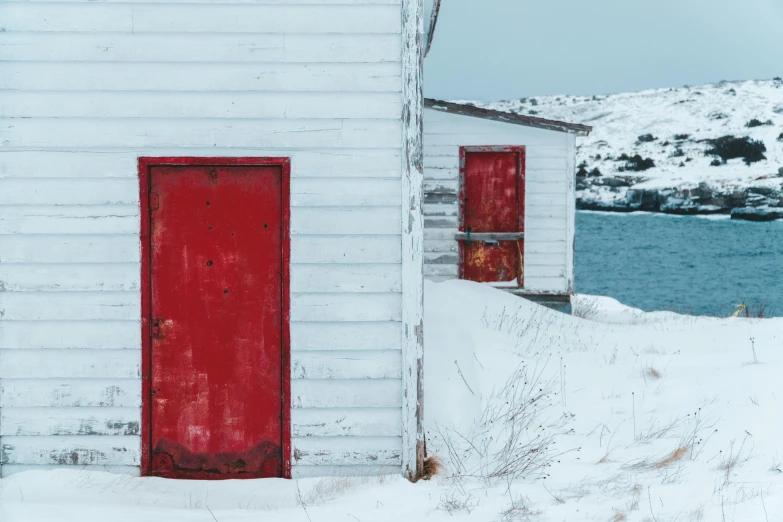 a white house with a red door in the snow, a photo, pexels contest winner, visual art, coastal, shack close up, 3 doors, vibrant but dreary