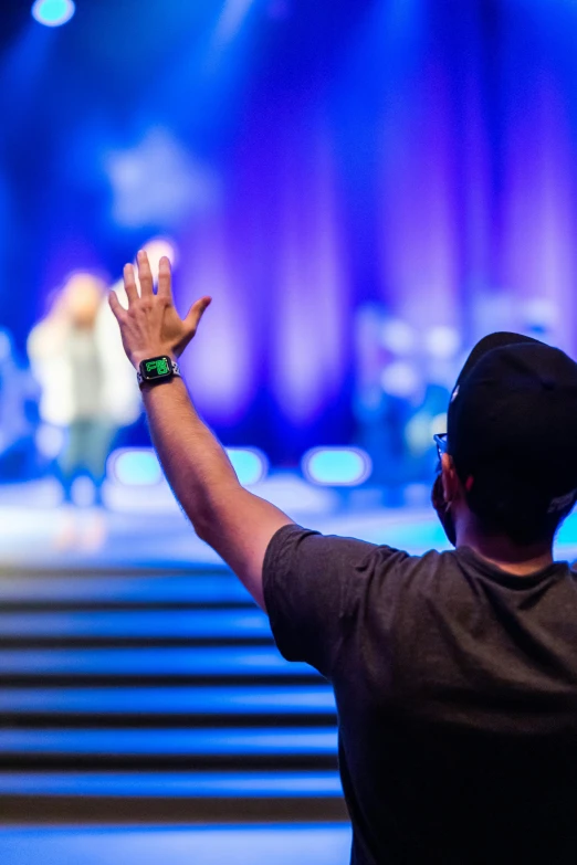 a man standing in front of a stage with his hands in the air, by Dan Content, church background, dabbing, comforting, people at work