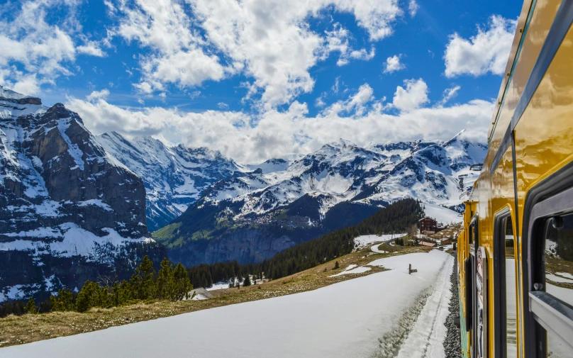 a yellow train traveling down a snow covered mountain side, by Daniel Seghers, pexels contest winner, art nouveau, snow capped mountains, conde nast traveler photo, slide show, panorama