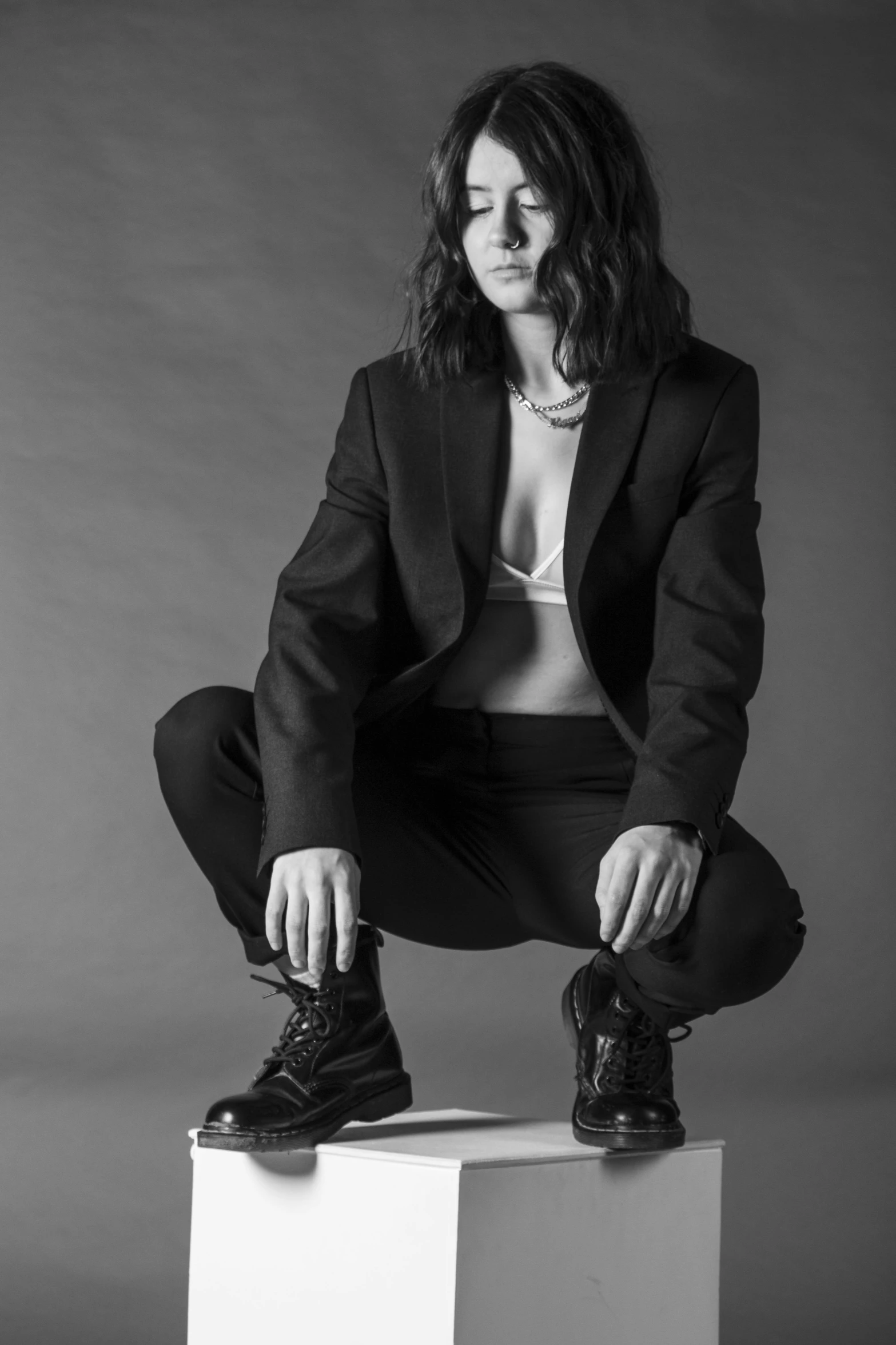 a woman sitting on top of a white box, a black and white photo, unsplash, antipodeans, ville valo, girl in a suit, yennefer, androgynous male