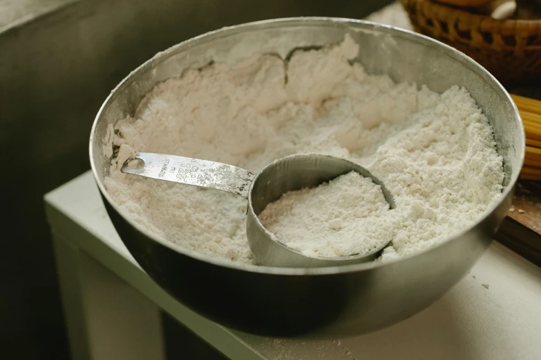 a metal bowl filled with flour sitting on top of a counter, food, piping, thumbnail, spoon