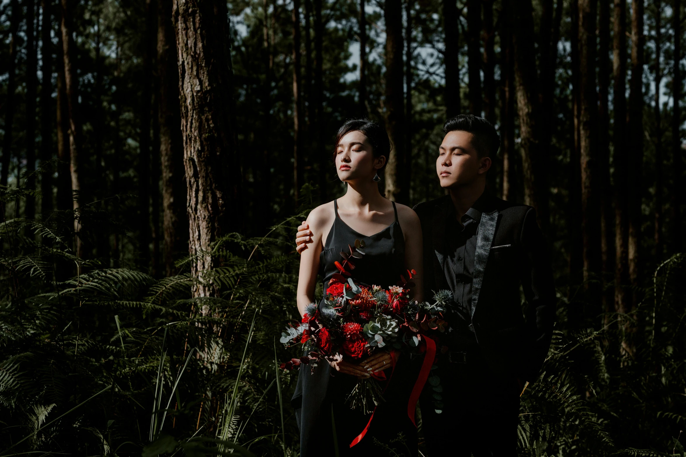 a man and woman standing next to each other in a forest, a portrait, pexels contest winner, black and red suit, bouquet, avatar image, hoang long ly