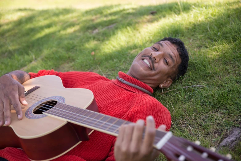 a man laying in the grass with a guitar, inspired by Ismail Gulgee, head bent back in laughter, production still, colour photograph, close - up photograph