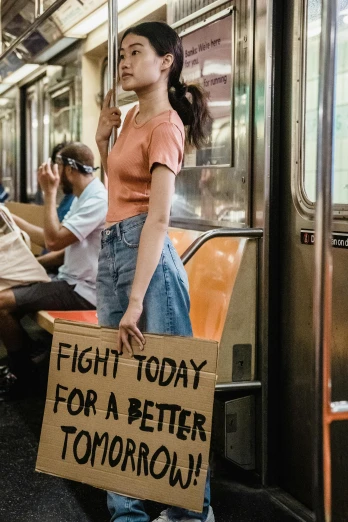 a woman holding a sign that says fight today for a better tomorrow, by Niko Henrichon, trending on unsplash, feminist art, subways, new york times, 256435456k film, teenager