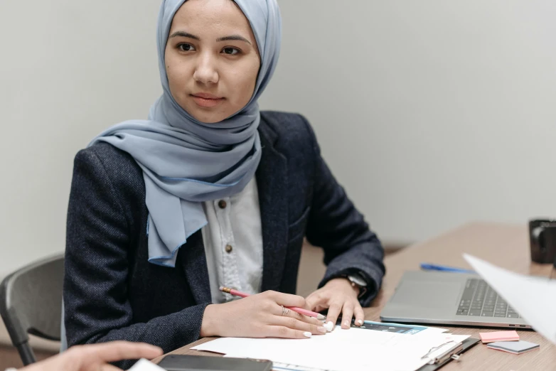 a woman in a headscarf sitting at a table, professional image, thumbnail, in a classroom, professional profile photo