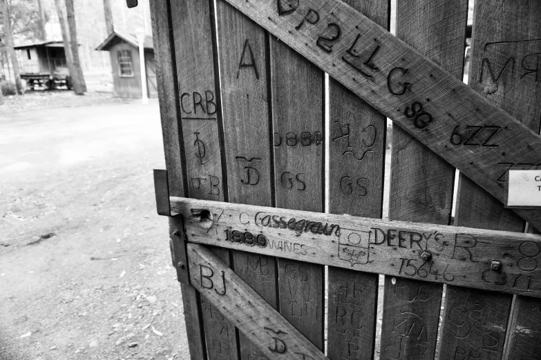 a black and white photo of a wooden gate, graffiti, letterboxing, with names, close up photo, derse