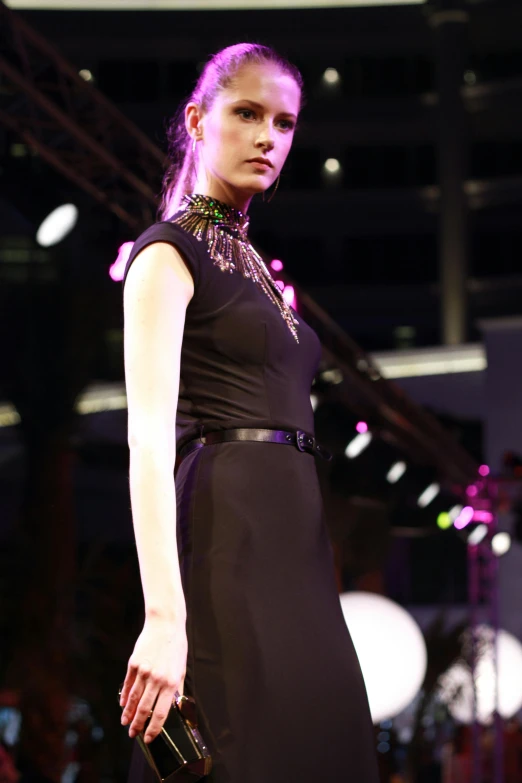 a woman in a black dress walking down a runway, wearing black choker, neon color details, (((dark colors))), on display