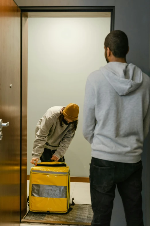 a couple of men standing next to each other in an elevator, process art, delivering parsel box, wearing a yellow hoodie, apartment hallway, repairing the other one