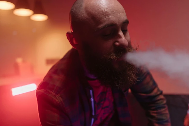 a man with a beard smoking a cigarette, with red haze, holding a small vape, bald man, multiple lights