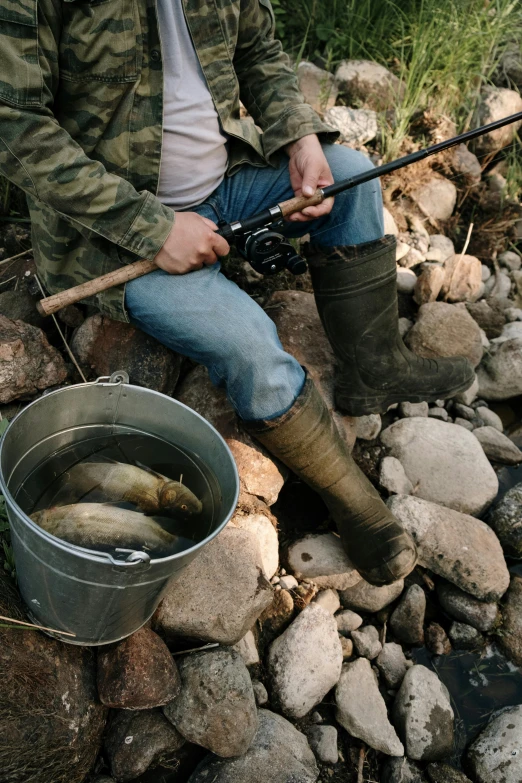 a man holding a fishing rod next to a bucket of fish, creeks, trout sticking out of pants, 2019 trending photo, canvas