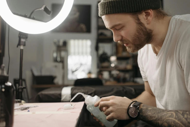 a man sitting at a table working on something, an airbrush painting, inspired by Seb McKinnon, trending on pexels, full scene shot, cutest, tattoo, white ink