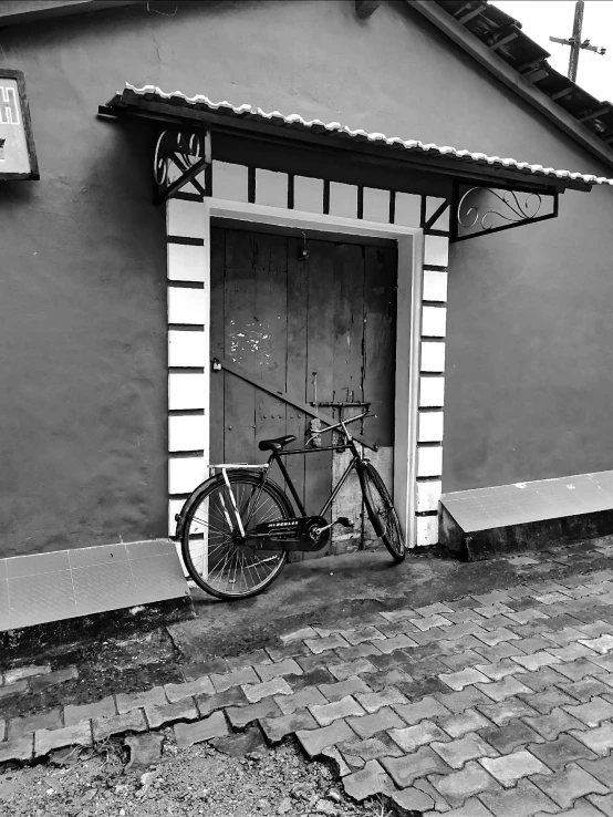a black and white photo of a bicycle parked in front of a building, a black and white photo, by Odhise Paskali, kerala village, cinematic. by leng jun, tall door, egor letov