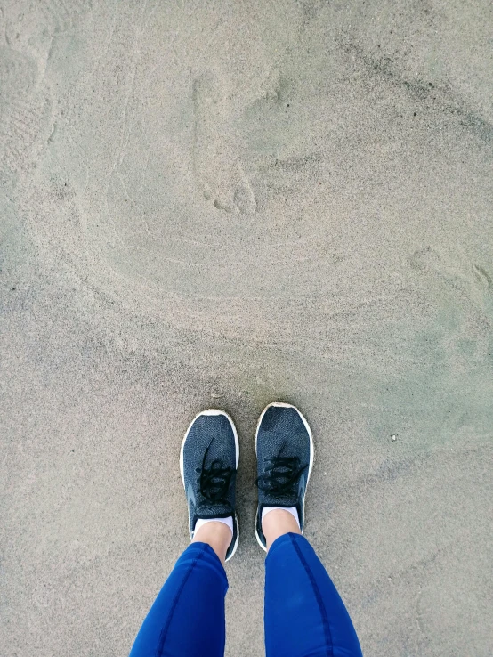 a person standing on top of a sandy beach, blue jeans and grey sneakers, snapchat photo, overcast day, top - down photograph