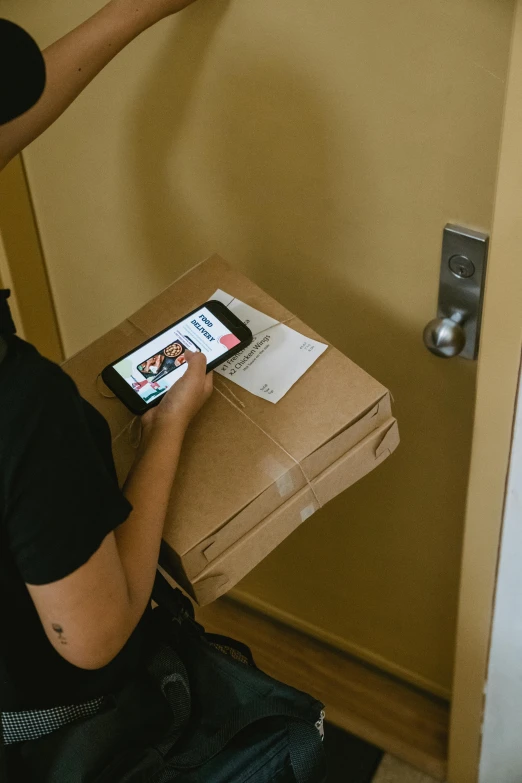 a man holding a cell phone in front of a box, hung above the door, profile image, cardboard, brown