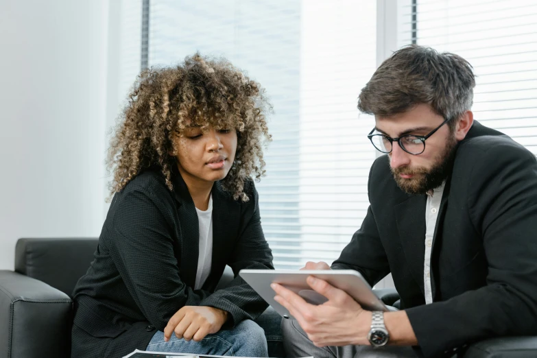 a man and woman sitting on a couch looking at a tablet, trending on pexels, professional profile picture, wearing causal black suits, it specialist, brown