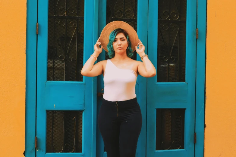 a woman standing in front of a blue door, inspired by Glòria Muñoz, pexels contest winner, aestheticism, wearing tight shirt, wearing sombrero, teal hair, dressed in a white t-shirt