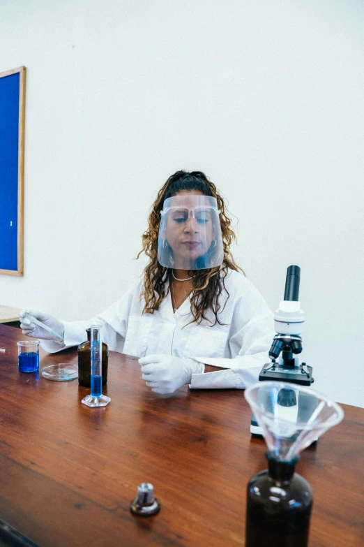 a woman sitting at a table in front of a microscope, an album cover, pexels, wearing transparent glass mask, in a classroom, taking mind altering drugs, clean medical environment