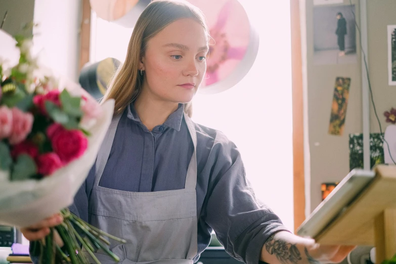a woman in an apron holding a bunch of flowers, a portrait, by Lee Loughridge, pexels contest winner, work clothes, at checkout, greta thunberg, looking across the shoulder
