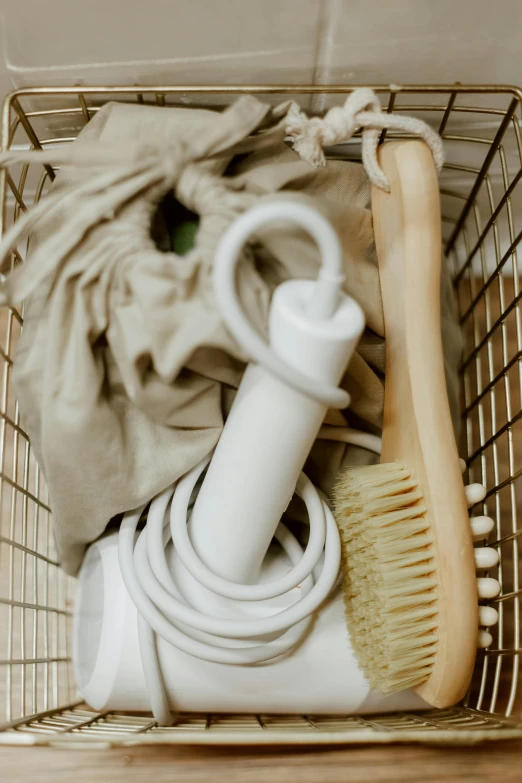 a basket filled with cleaning supplies on top of a wooden table, a portrait, inspired by Suzanne Duchamp-Crotti, unsplash, white broom closet, hairdryer, beige, close-up product photo