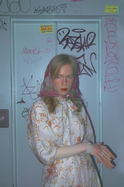 a woman standing in front of a door covered in graffiti, an album cover, inspired by Nan Goldin, tumblr, young nicole kidman, head scarf, duane hanson, super aesthetic