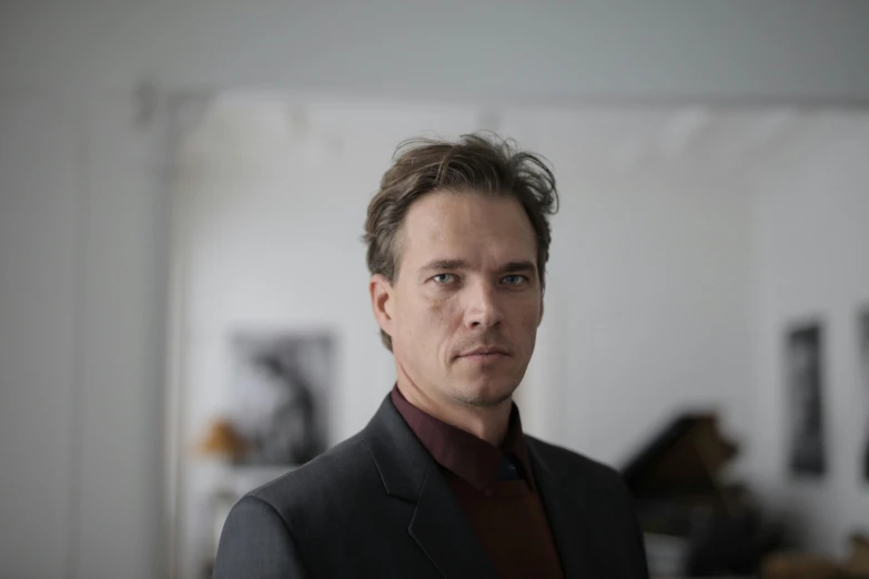 a man in a suit standing in a room, by Ejnar Nielsen, headshot photograph, wolfgang novogratz, composer, kirsi salonen