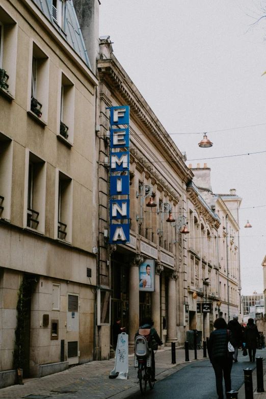 a group of people walking down a street next to tall buildings, trending on pexels, art nouveau, russian cinema, bright signage, french village exterior, selina