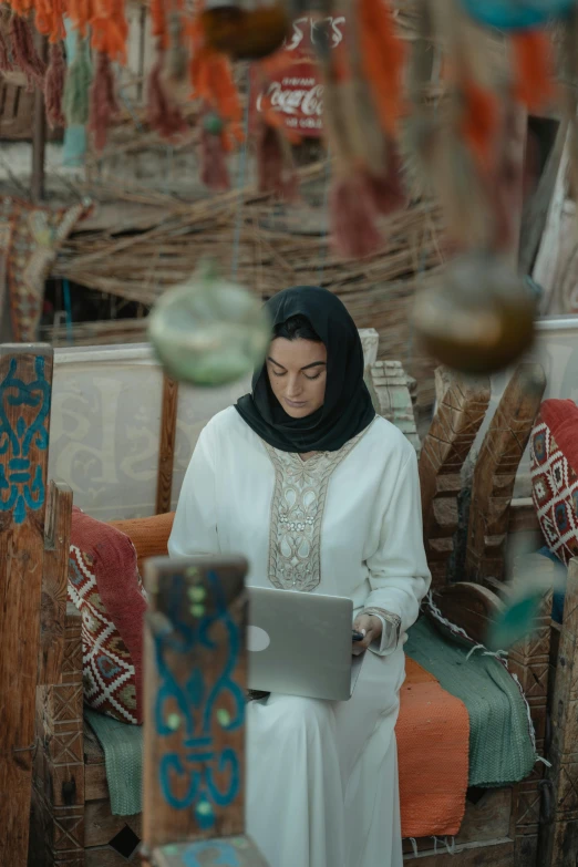 a woman in a white dress using a laptop, inspired by Maryam Hashemi, trending on pexels, hurufiyya, inside an arabian market bazaar, ( ( theatrical ) ), rustic, tech robes