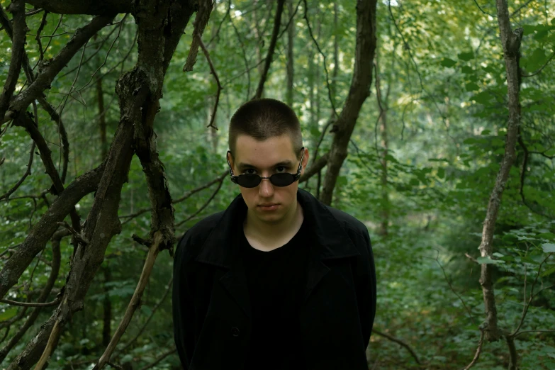 a man standing in the woods with a frisbee, an album cover, inspired by Jean Malouel, unsplash, purism, dark glasses, brown buzzcut, portrait shot 8 k, underworld