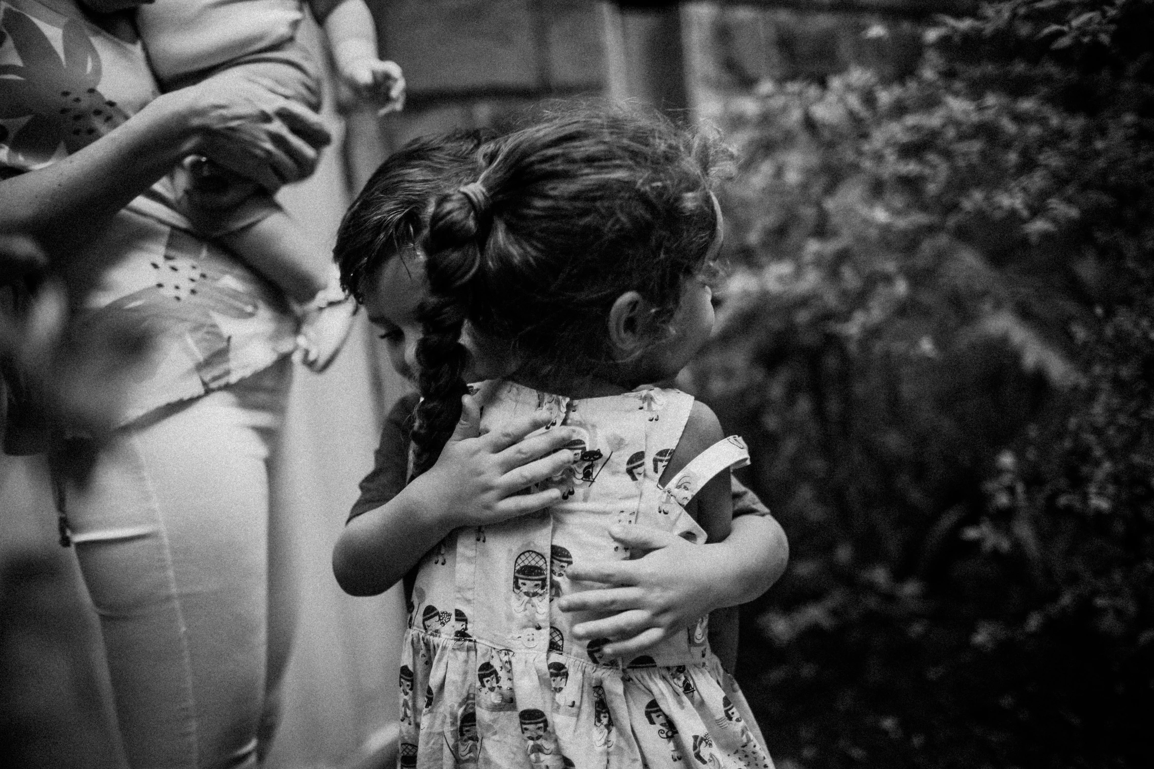 a black and white photo of a little girl hugging her mother, pexels, standing with her back to us, 8k 50mm iso 10, two girls, patterned