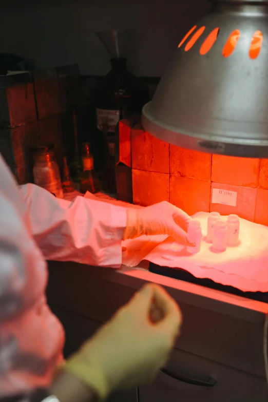 a man that is standing in front of a stove, pathology sample test tubes, warm lighting inside, partially cupping her hands, ambient cave lighting