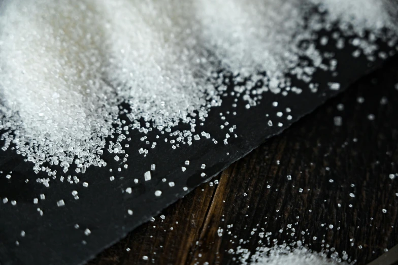 a pile of sugar sitting on top of a wooden table, a microscopic photo, trending on pexels, beaded embroidery, background image, alessio albi, powdered sugar