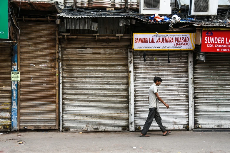 a man walking down a street past a building, trending on unsplash, madhubani, boarded up, stores, thumbnail