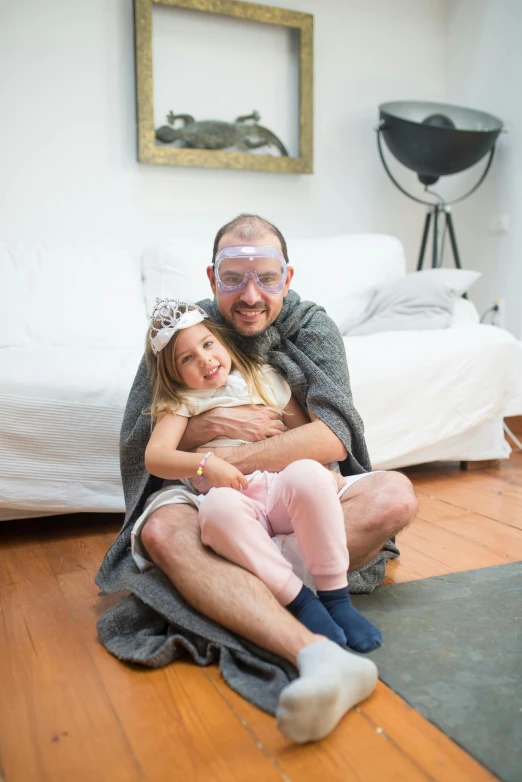 a man and a little girl sitting on the floor, a picture, inspired by Leo Leuppi, featured on reddit, dada, wearing nanotech honeycomb robe, with glasses and goatee, covered in bandages, high res photograph