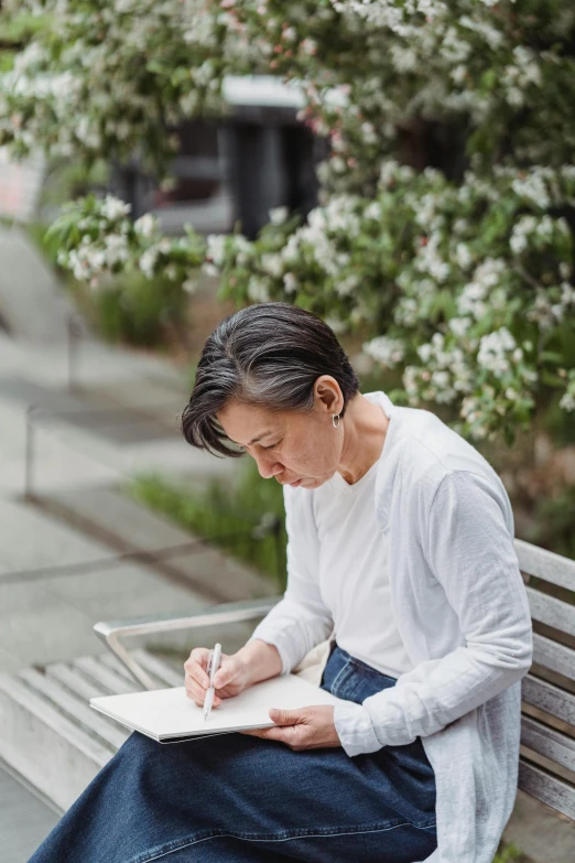 a woman sitting on a bench writing on a piece of paper, inspired by Ruth Jên, artist arata yokoyama, al fresco, 2019 trending photo, architect