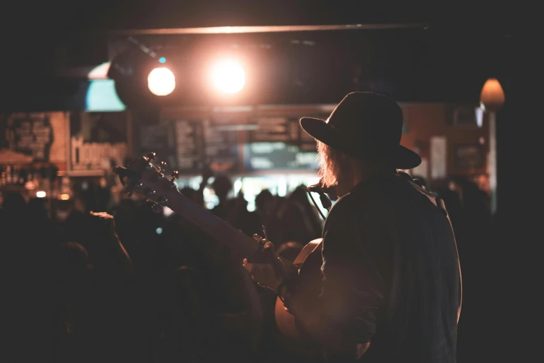 a man playing a guitar in front of a crowd, pexels contest winner, dimly lit cozy tavern, hazy, willie nelson on stage, lachlan bailey