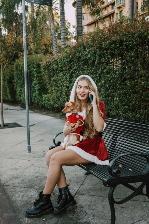 a woman sitting on a bench talking on a cell phone, an album cover, by Julia Pishtar, pexels, renaissance, wearing festive clothing, holding paws, red short dress, california;