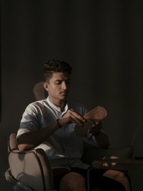 a man sitting in a chair holding a paddle, by Ahmed Yacoubi, pexels contest winner, hurufiyya, male teenager, soft light.4k, dimly light room, ( ( theatrical ) )