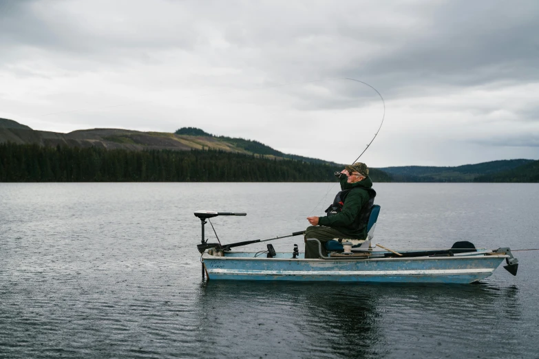 a man sitting in a small boat on a lake, by Jessie Algie, pexels contest winner, fishing pole, grey, montana, where a large