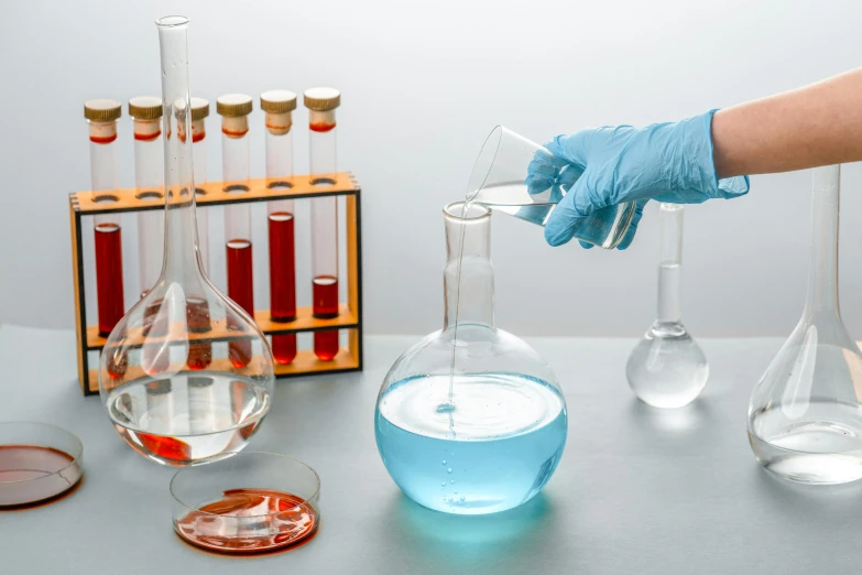 a close up of a person holding a beaker filled with liquid, vermillion and cyan, vases and bottles, chemrail, tabletop