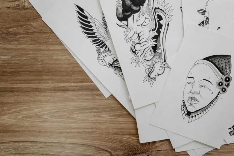 a bunch of cards sitting on top of a wooden table, an ink drawing, by Daniel Lieske, trending on pexels, hyper - realistic tattoo sketch, drawn on white parchment paper, portrait close - up, flat linework