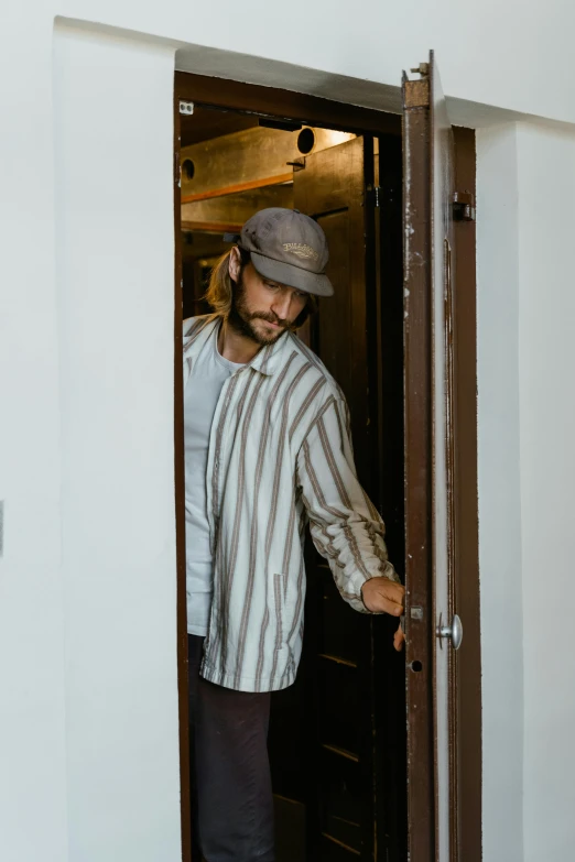 a man that is standing in a doorway, striped shirt, caracter with brown hat, zachary corzine, ignant