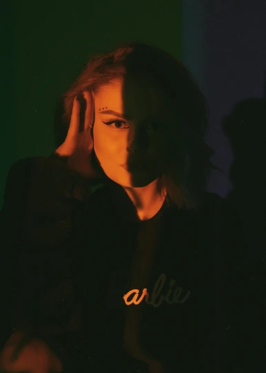 a woman sitting in a dark room with her hand on her head, an album cover, inspired by Elsa Bleda, trending on pexels, realism, made of neon light, portrait of annasophia robb, in a black hoodie, alive